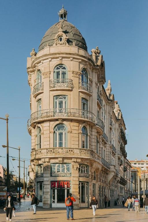 Historic architectural building intersection in Lisbon under clear blue sky, with pedestrians walking nearby.