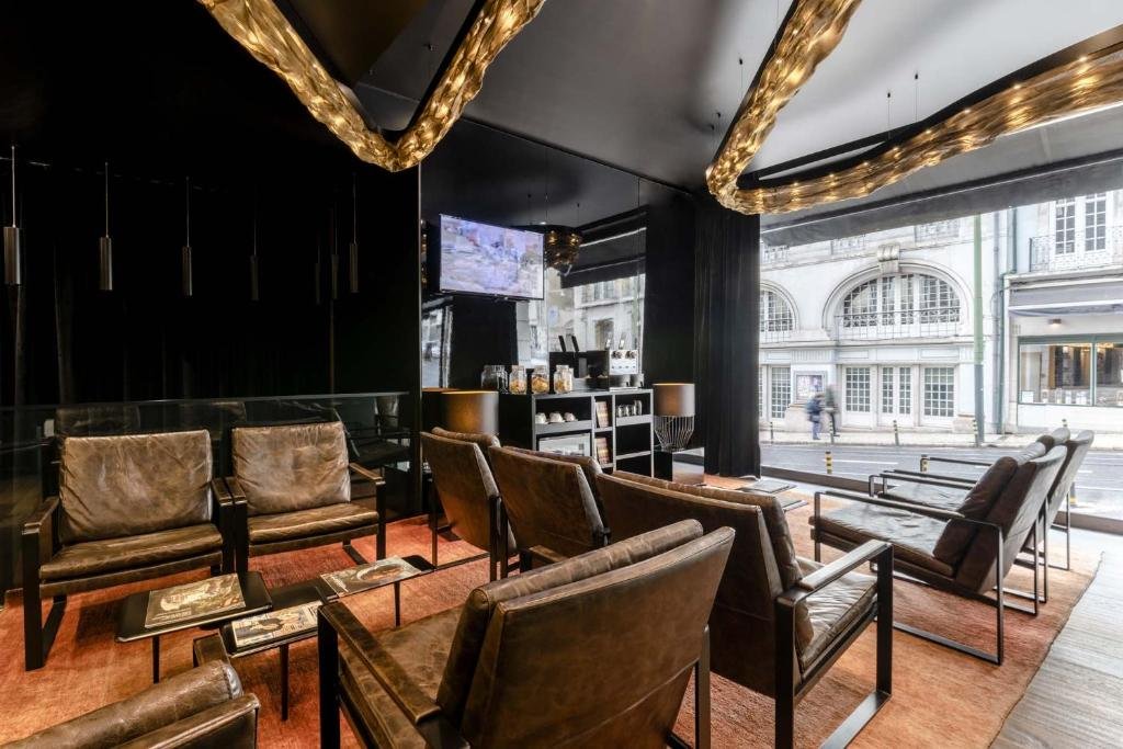 Modern hotel lobby with leather seating, large windows, stylish lighting, and a street view for a cozy guest experience.