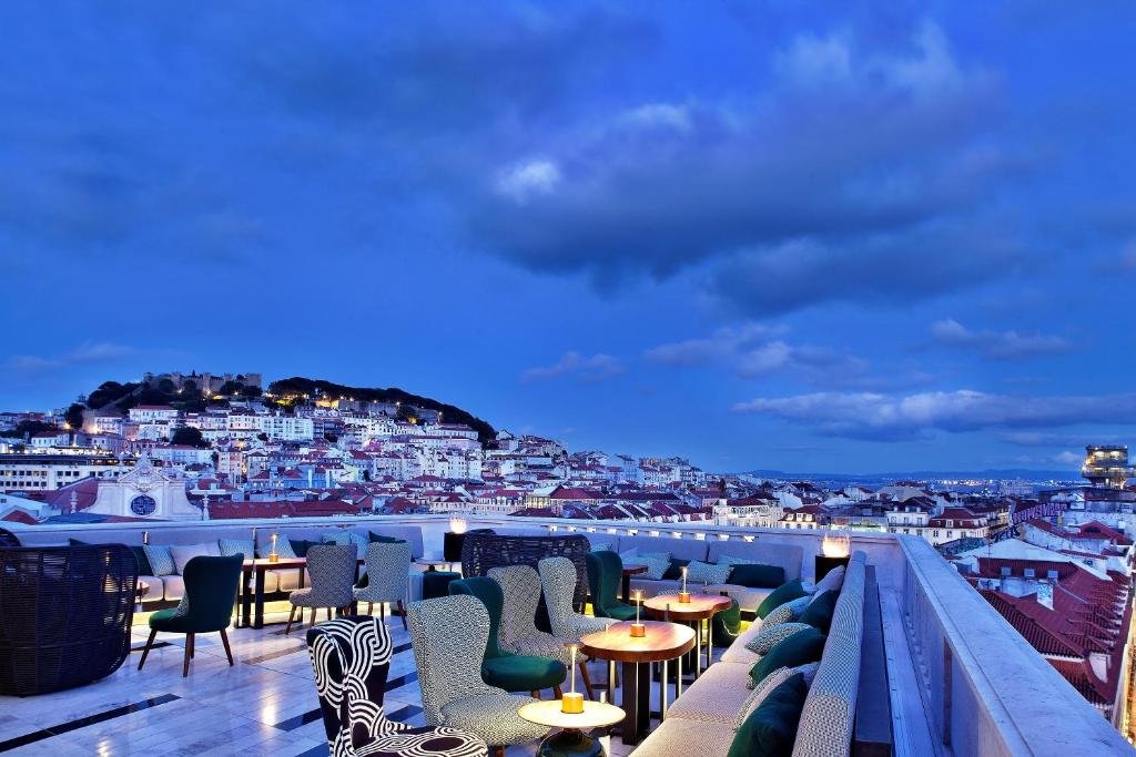 Rooftop terrace with city view at sunset, featuring cozy seating and ambient lighting under a vibrant blue sky.
