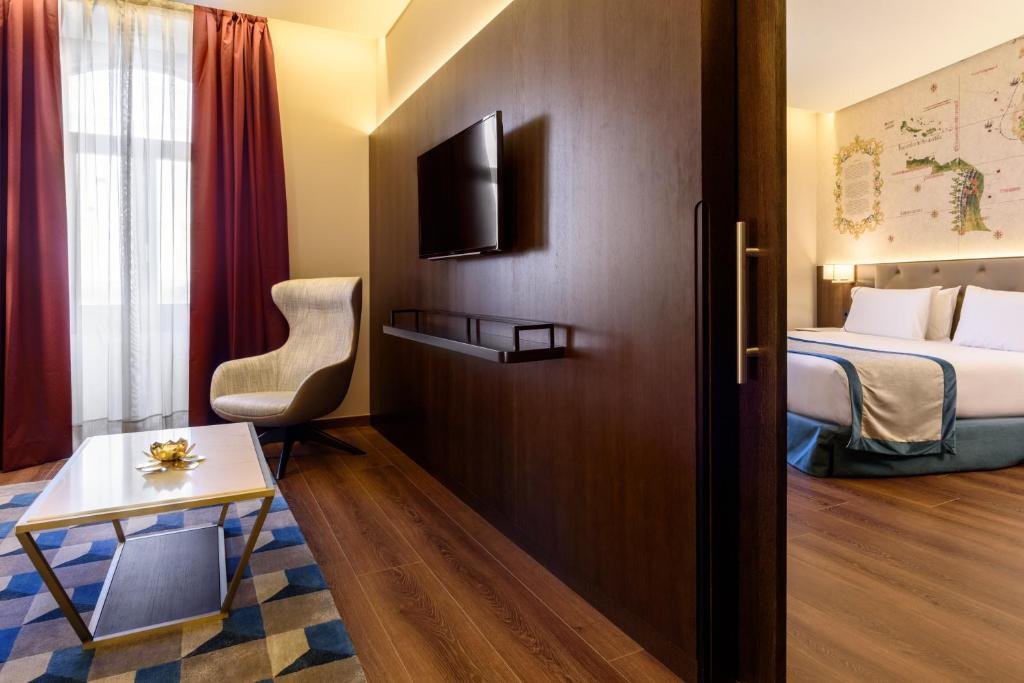Modern hotel suite with comfortable seating, wall-mounted TV, and cozy bed, perfect for a relaxing stay.