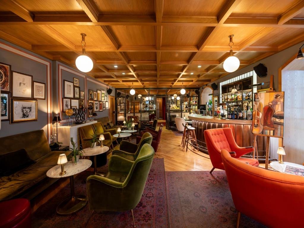 Cozy vintage bar interior with colorful seating, framed artwork, and warm lighting creating an inviting atmosphere.