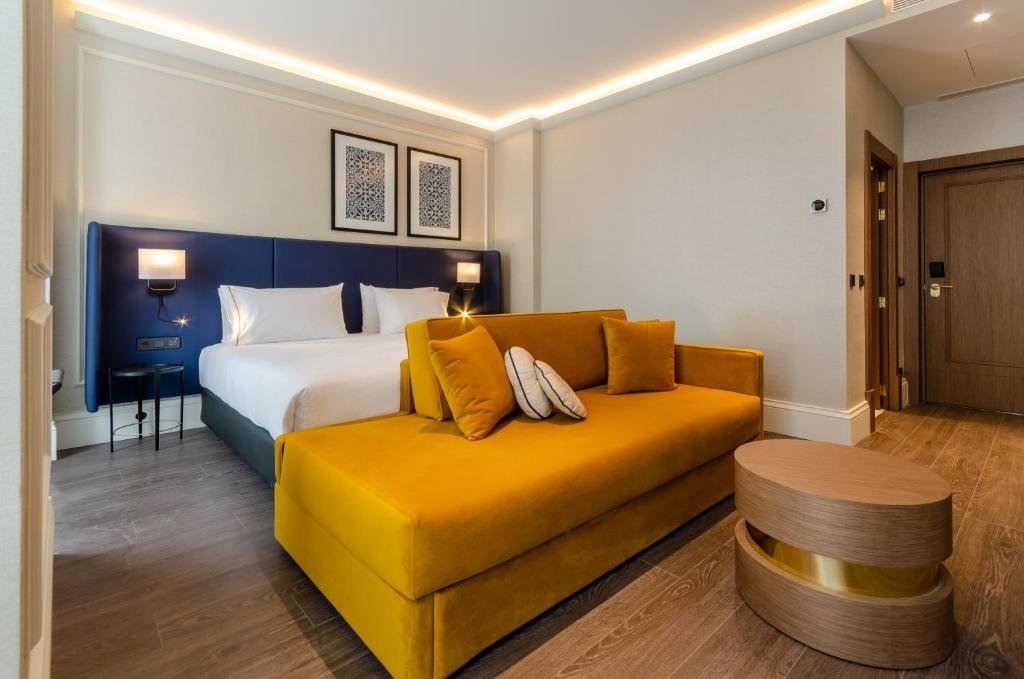 Modern hotel room with a comfortable bed, stylish mustard yellow sofa, and elegant decor.