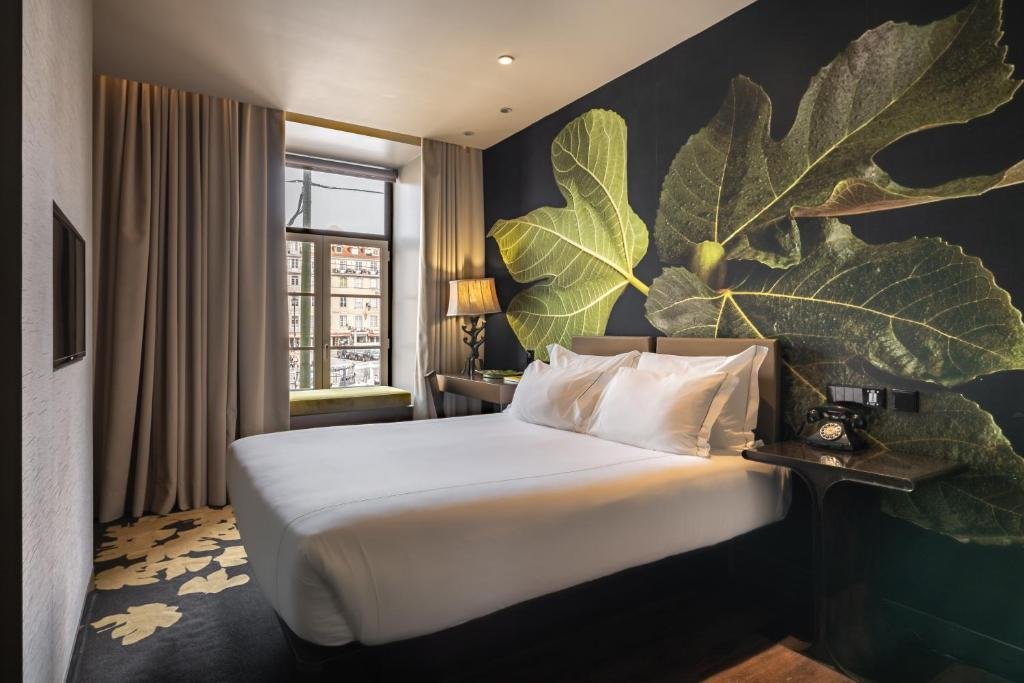 Modern hotel room with leafy wall art, cozy bed, vintage phone, and city view window. Warm lighting and elegant decor.