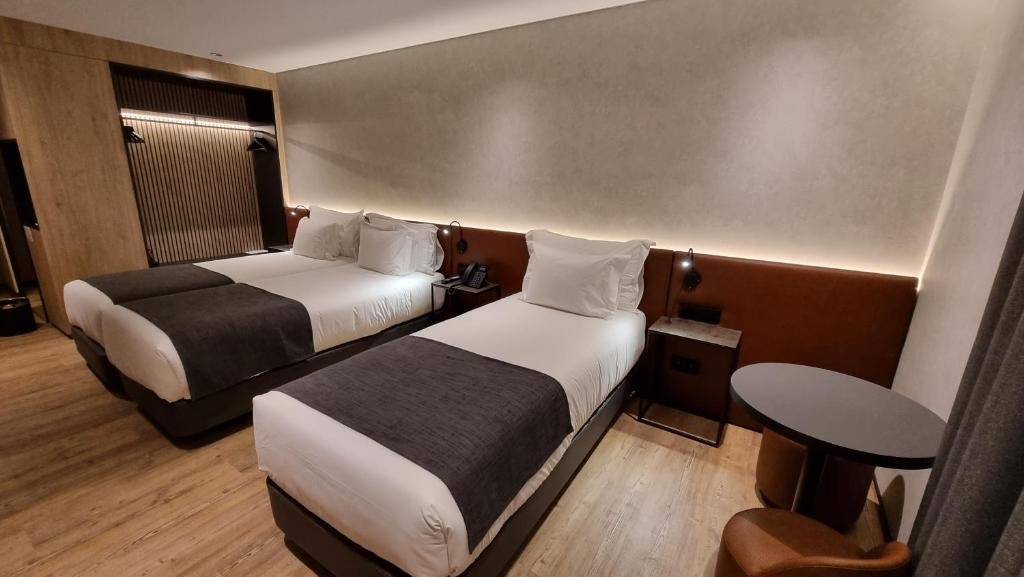 Modern hotel room with two twin beds, plush linens, wooden floor, and a cozy seating area.