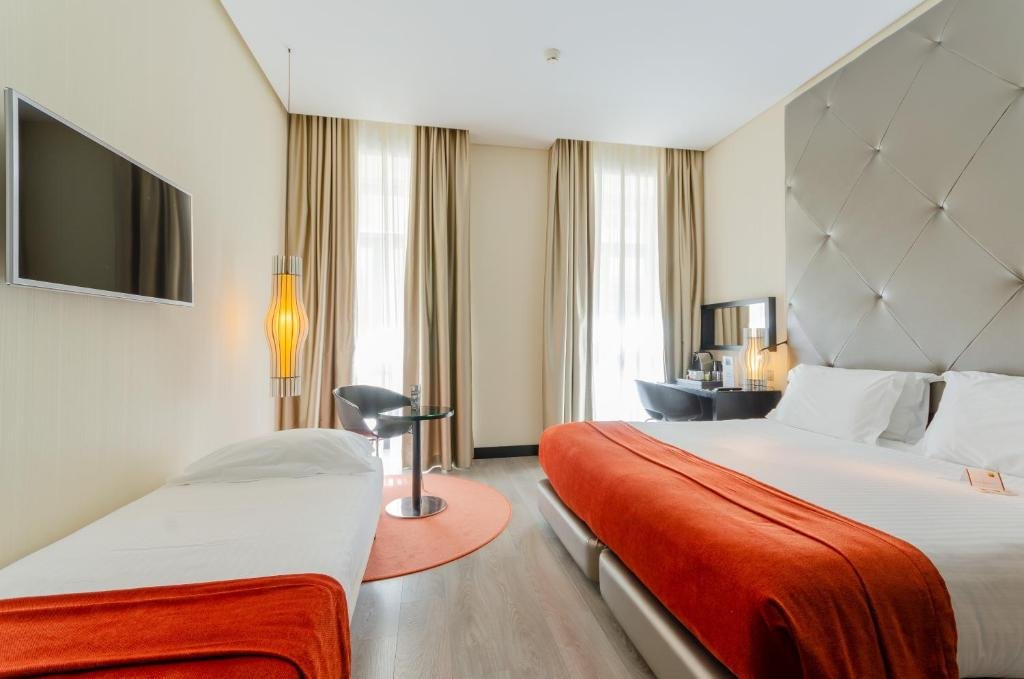 Modern hotel room with a double bed, red accents, flat-screen TV, and elegant decor.