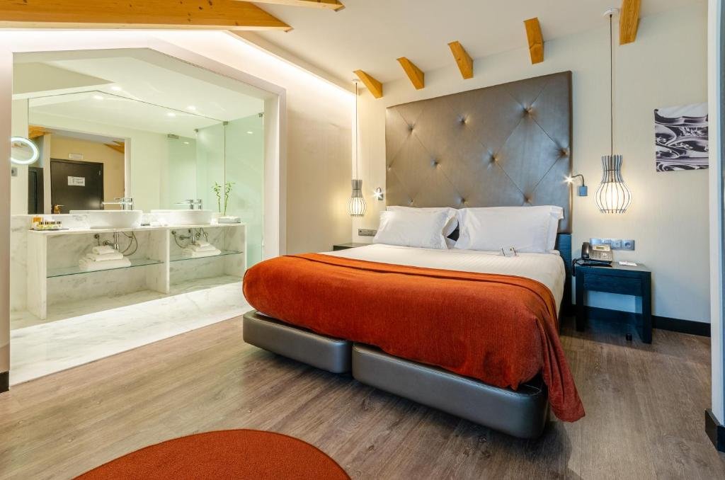 Modern hotel room with orange bedspread, elegant lighting, and spacious en-suite bathroom with double sinks.