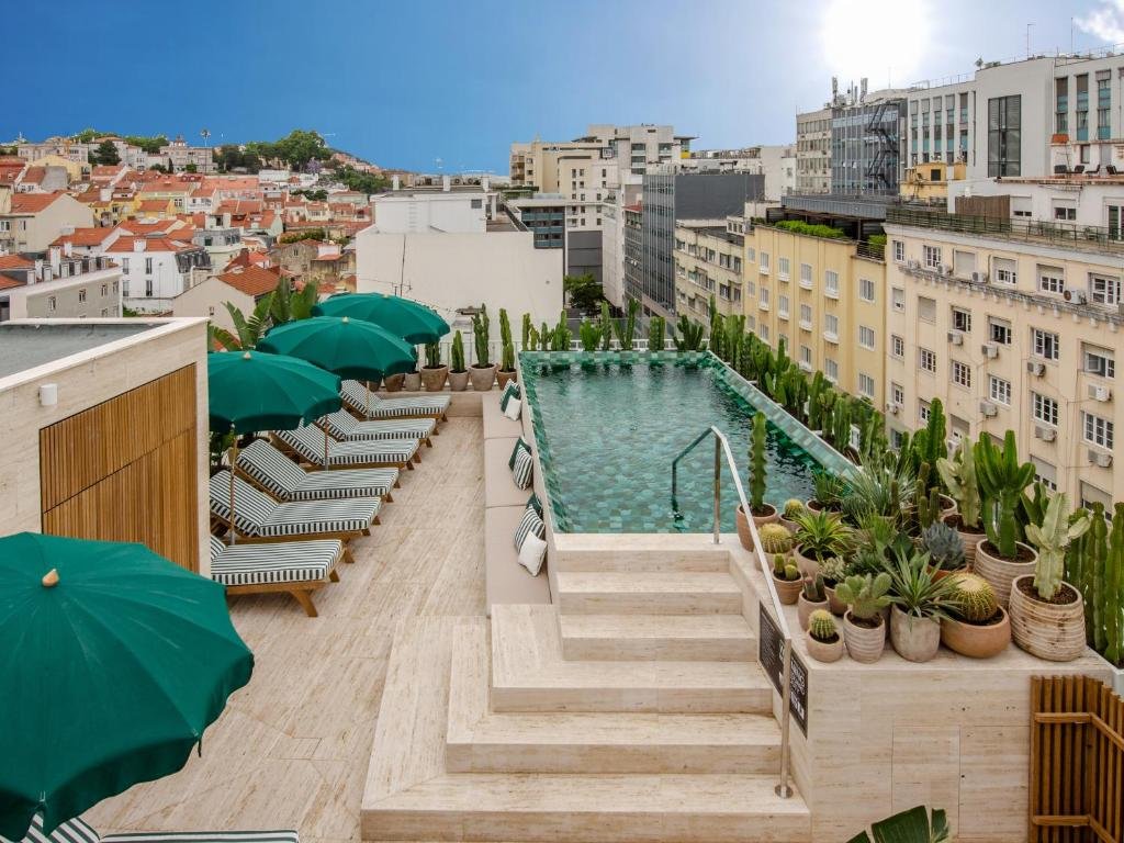 Rooftop pool with green umbrellas and lush plants overlooking a cityscape on a sunny day.