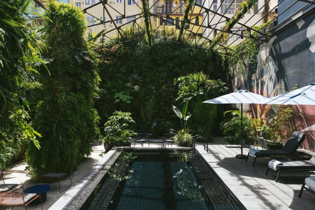 Outdoor urban oasis with lush vertical garden, small pool, lounge chairs, and umbrellas in a cozy courtyard setting.