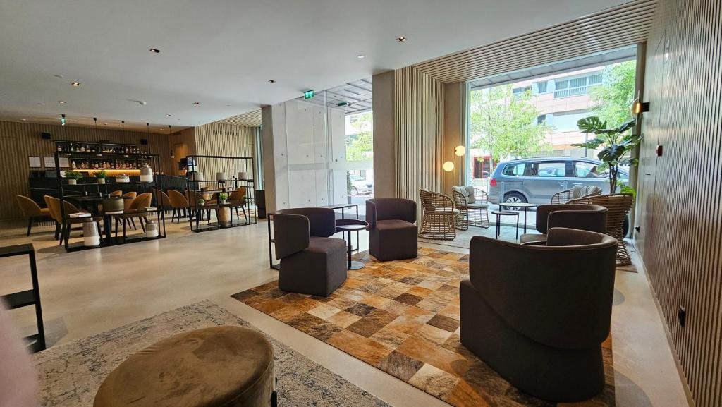 Modern hotel lobby with cozy seating, bar area, and large windows overlooking a tree-lined street.