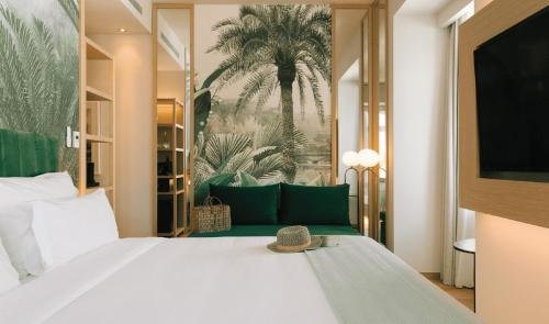 Modern hotel room with tropical-themed decor, featuring a palm tree mural, plush green seating, and cozy bedding.