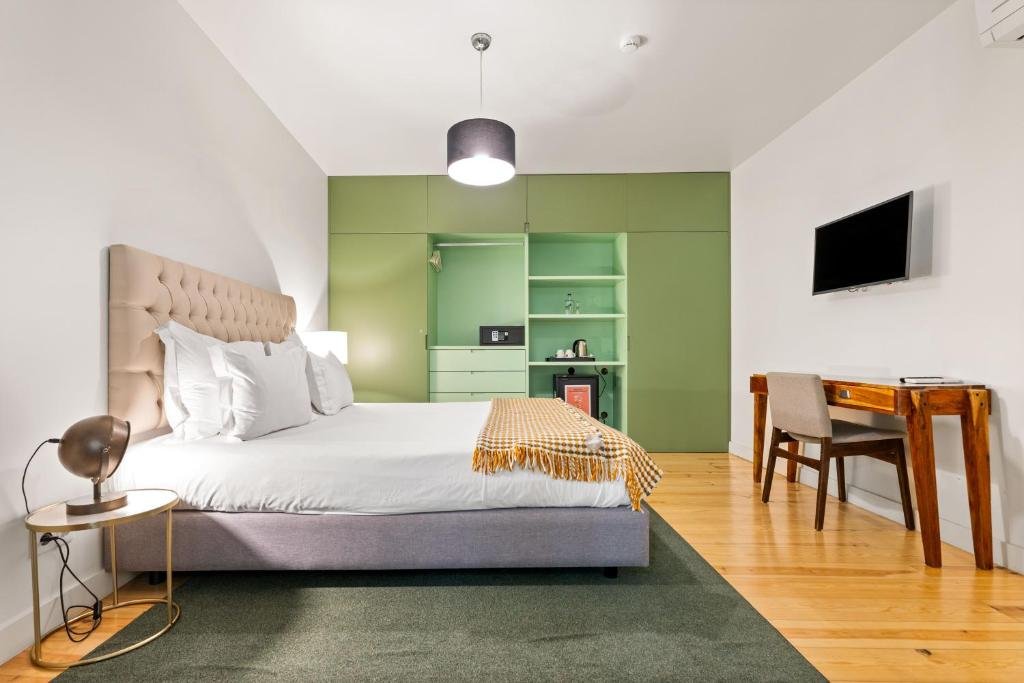 Modern hotel room with king bed, green accent wall, wooden desk, and wall-mounted TV. Cozy and stylish interior.
