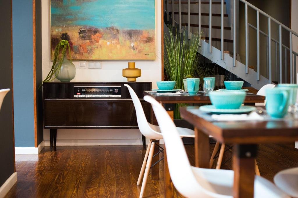 Modern dining room with turquoise tableware, abstract art, and mid-century decor near a staircase.