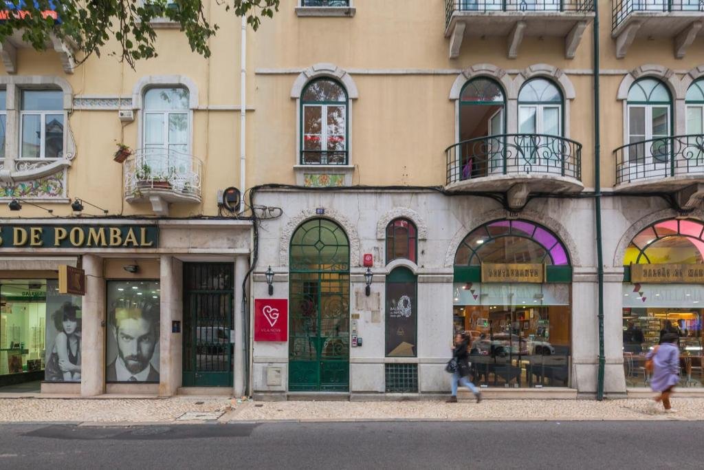 Historic Lisbon building facade with arched windows and shops at street level, pedestrians walking by.