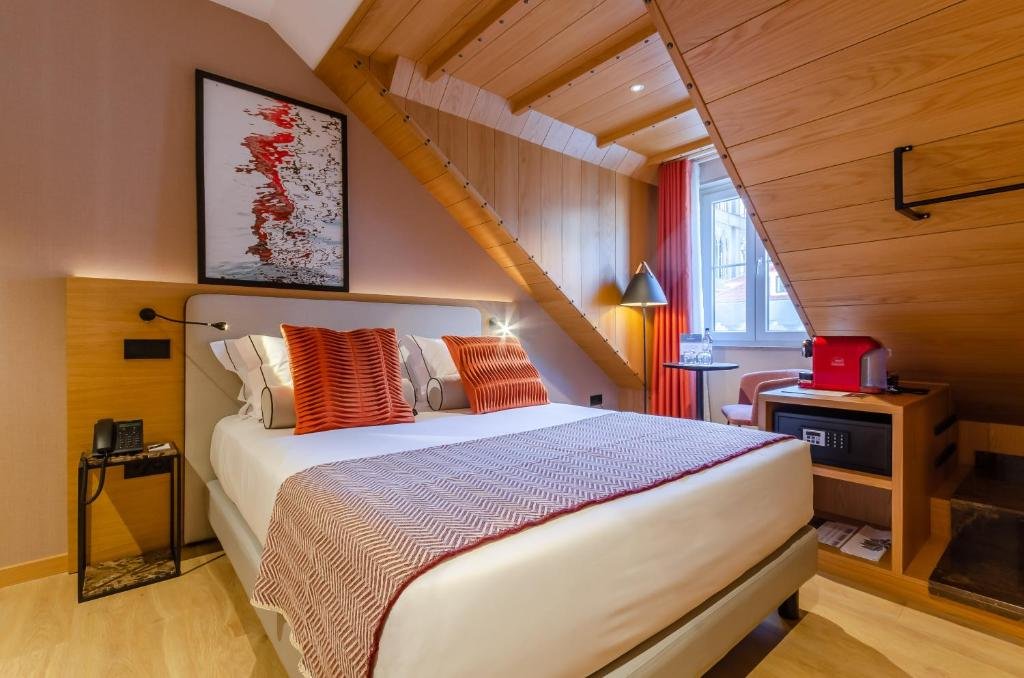 Cozy attic bedroom with modern decor, double bed, vivid pillows, red accents, and a sloping wooden ceiling.