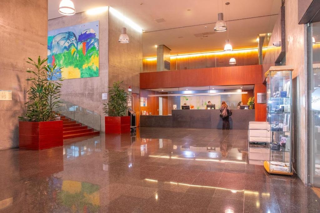 Modern hotel lobby with artwork, reception desk, and glass display case, featuring warm lighting and sleek decor.