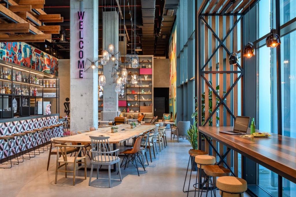 Modern cafe interior with colorful decor, long wooden tables, bar area, and natural light from large windows.