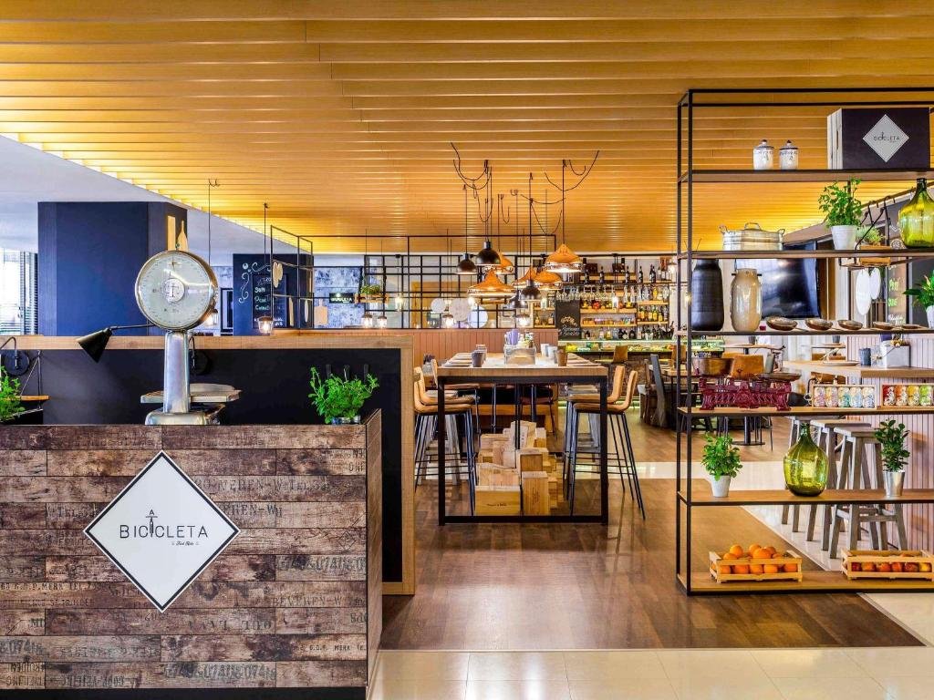 Modern restaurant interior with wooden accents, shelves displaying decor and plants, and a welcoming dining atmosphere.