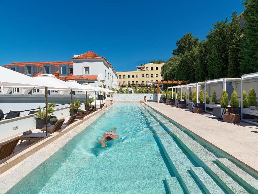 Luxurious hotel pool area with lounge chairs, umbrellas, and cabanas under a clear blue sky.