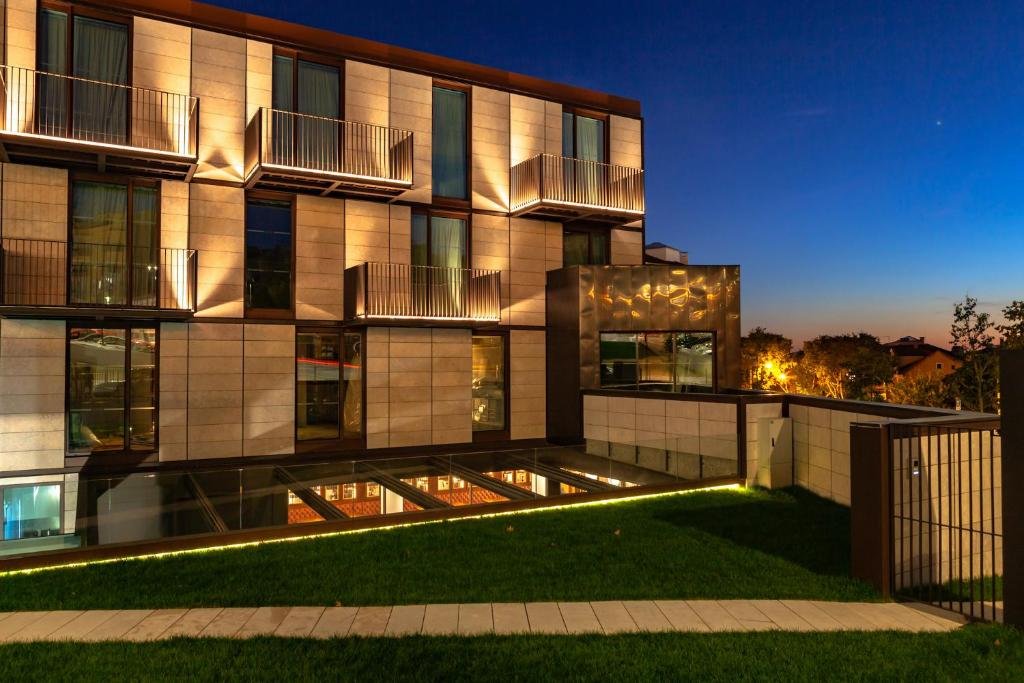 Modern building exterior at night, featuring illuminated balconies and a landscaped garden against a twilight sky.