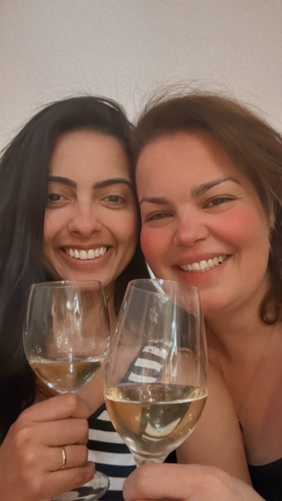 Two smiling women toasting with glasses of white wine, enjoying a happy moment together.