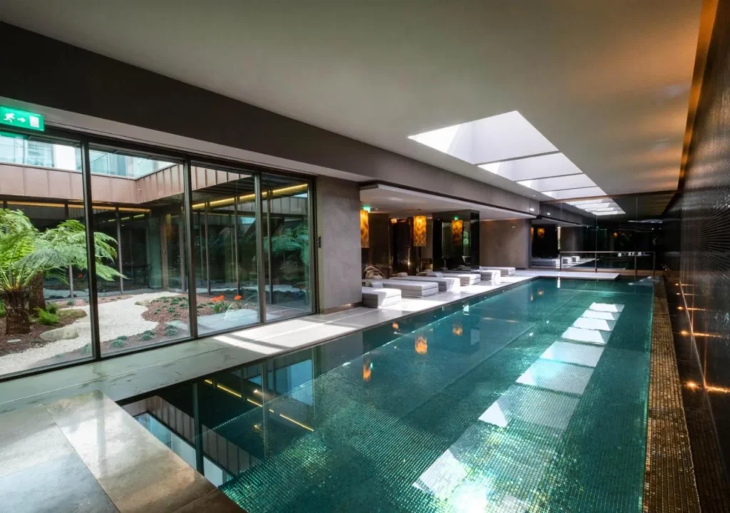Luxurious indoor swimming pool with natural light, modern design, and lush garden view through large windows.