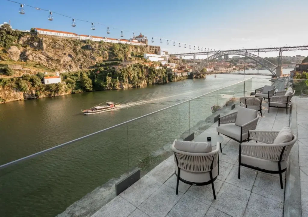 Scenic river view from a modern terrace with cozy seating, overlooking a bridge and a hillside in the background.