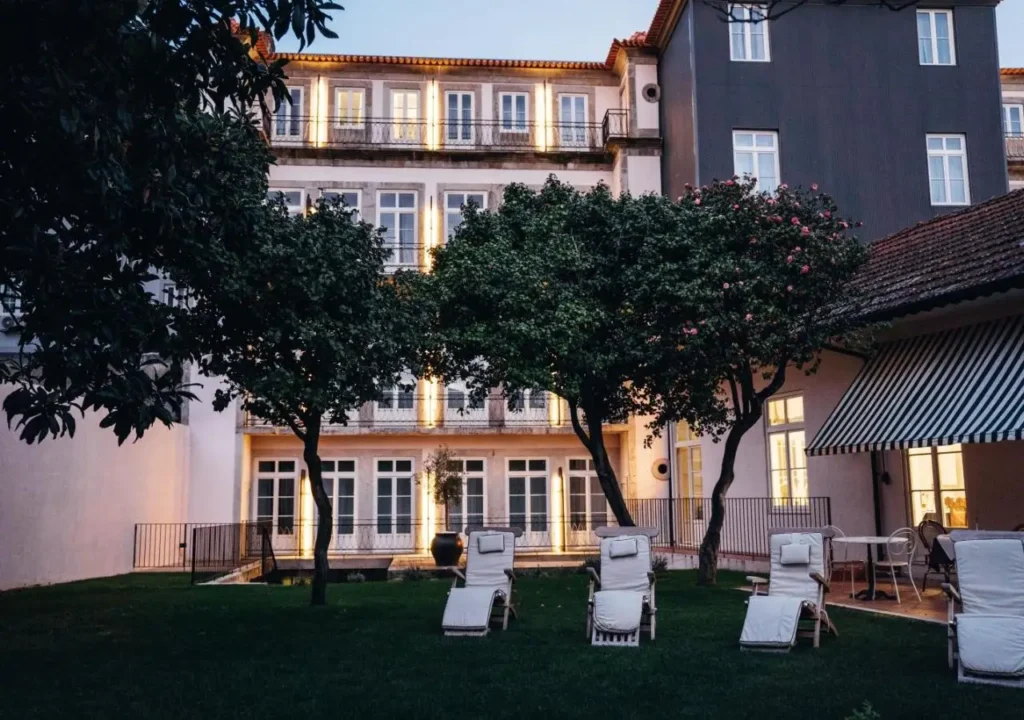 Elegant hotel exterior with lit windows and garden lounge chairs at dusk. Serene and inviting ambiance.