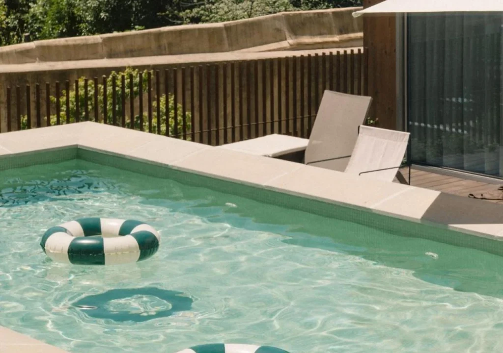 Sunny poolside with striped inflatable ring and lounge chairs near a modern wooden deck—perfect for relaxation.