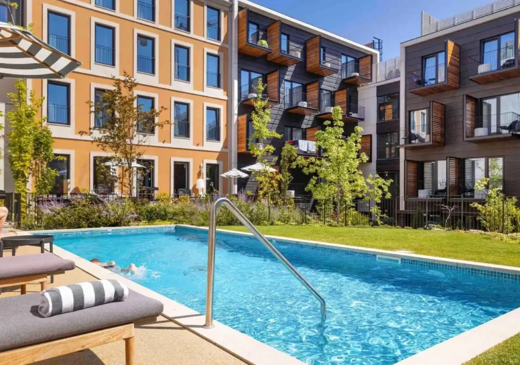 Modern apartment buildings with a relaxing outdoor pool area and green landscaping under a clear blue sky.