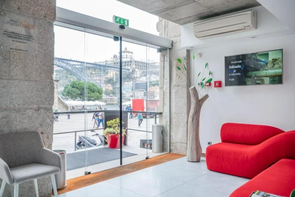 Modern hotel lobby with red seating and glass doors overlooking Porto's riverside and iconic bridge.