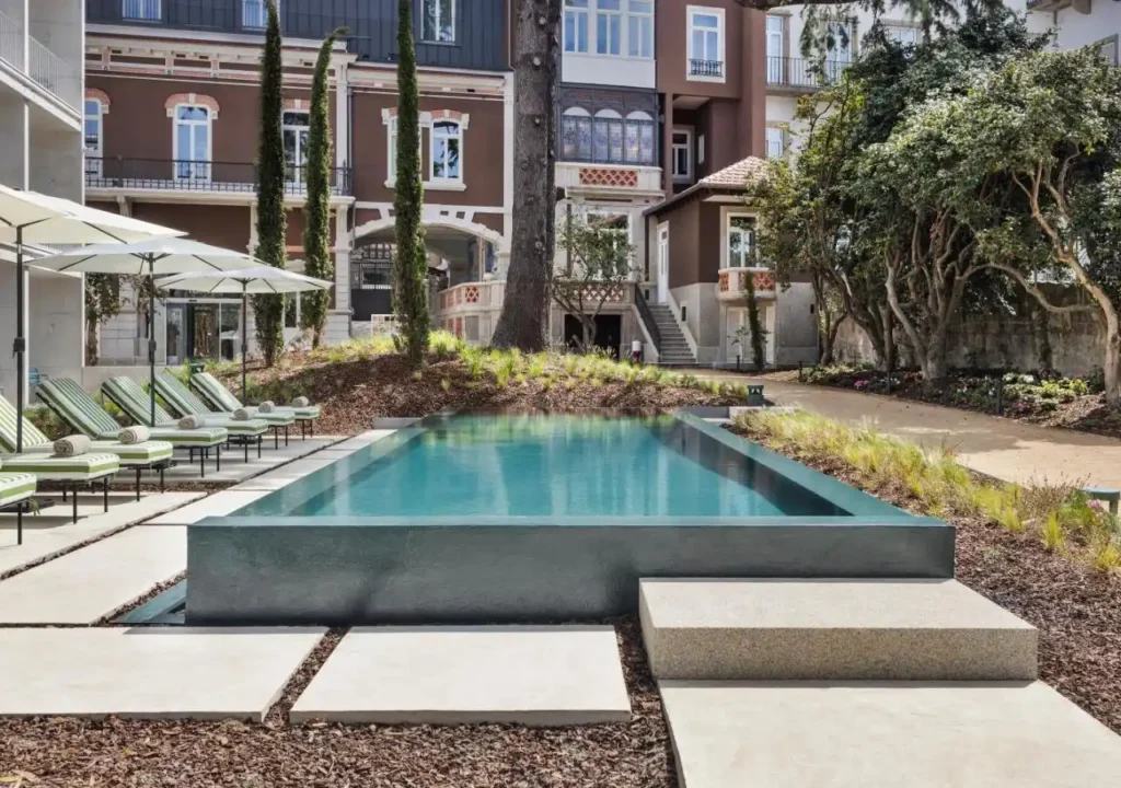 Luxury hotel pool with sun loungers, umbrellas, and elegant architecture in a serene garden setting.