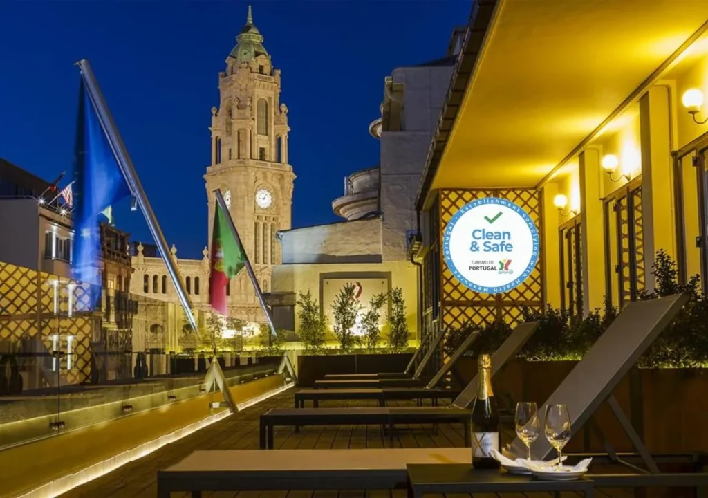 Rooftop terrace view of historical clock tower at night, with Clean & Safe sign in Portugal, wine on table.