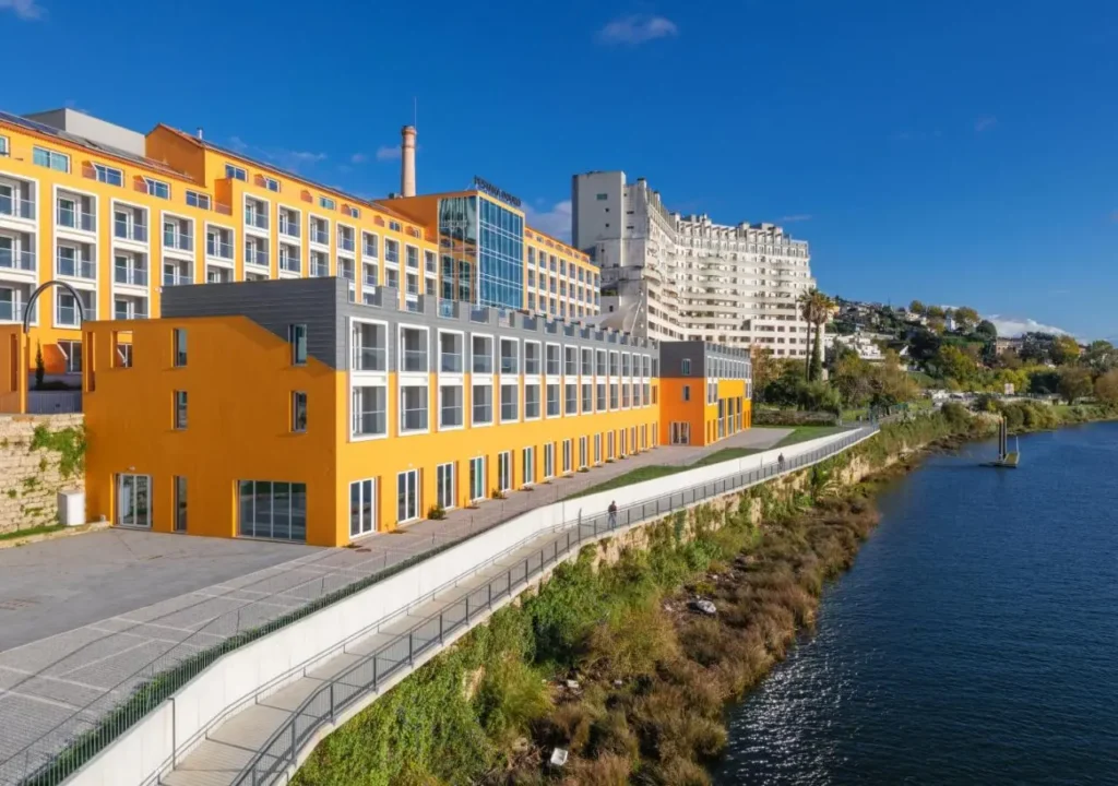 Bright yellow building with modern architecture along a river under a clear blue sky.