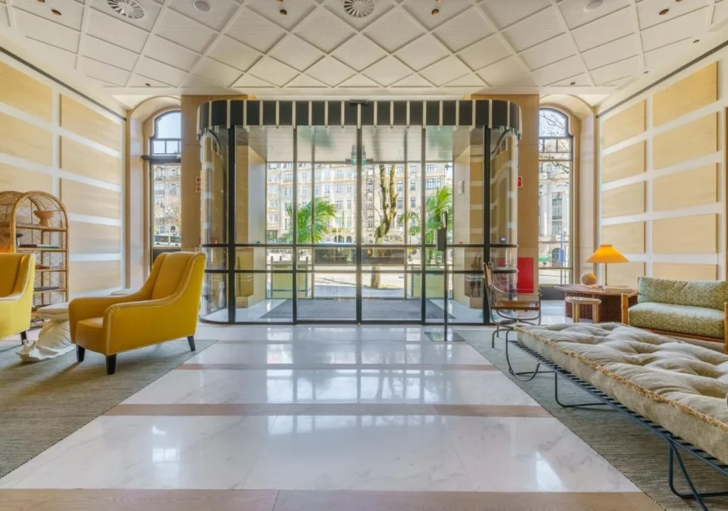 Modern hotel lobby with yellow chairs, a glass entrance, and outdoor view. Sophisticated design and bright atmosphere.
