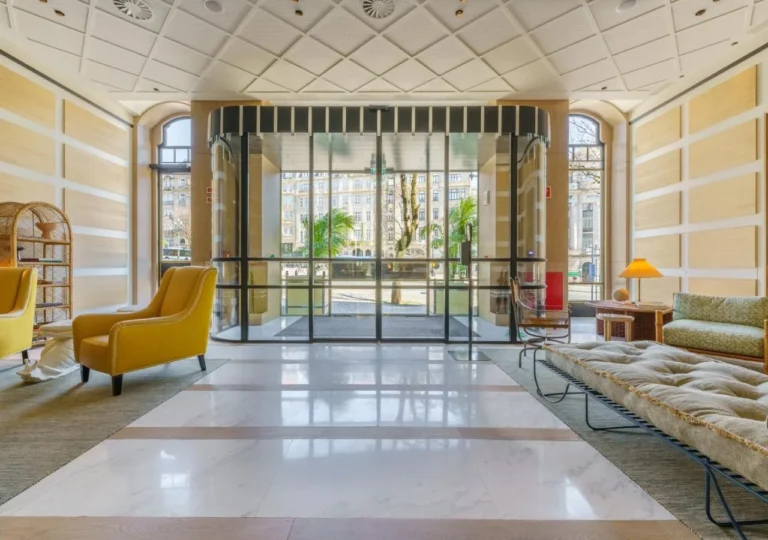 Modern hotel lobby with yellow chairs, a glass entrance, and outdoor view. Sophisticated design and bright atmosphere.