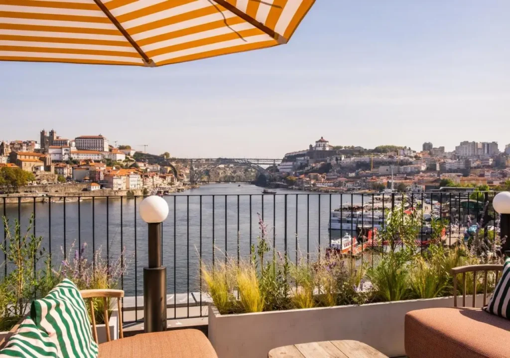 River view from a terrace with striped canopy in Porto, Portugal, featuring historic architecture and a bridge.