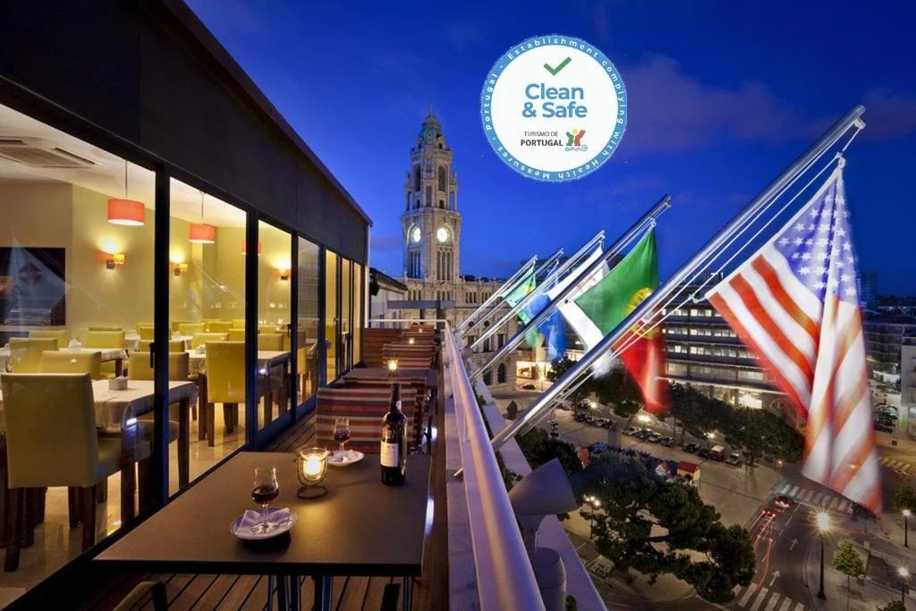 Rooftop dining with city view, flags, and Clean & Safe seal at dusk, featuring outdoor seating and elegant ambiance.