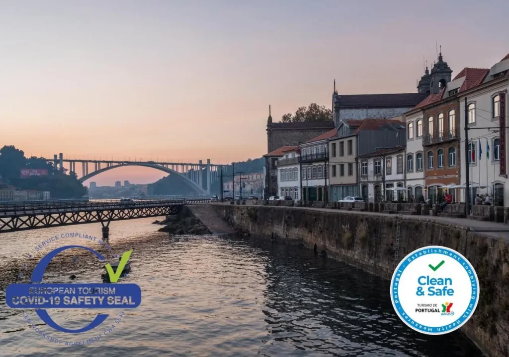 Sunset view of Porto riverside with bridge and COVID-19 safety seals, highlighting travel assurance in Portugal.