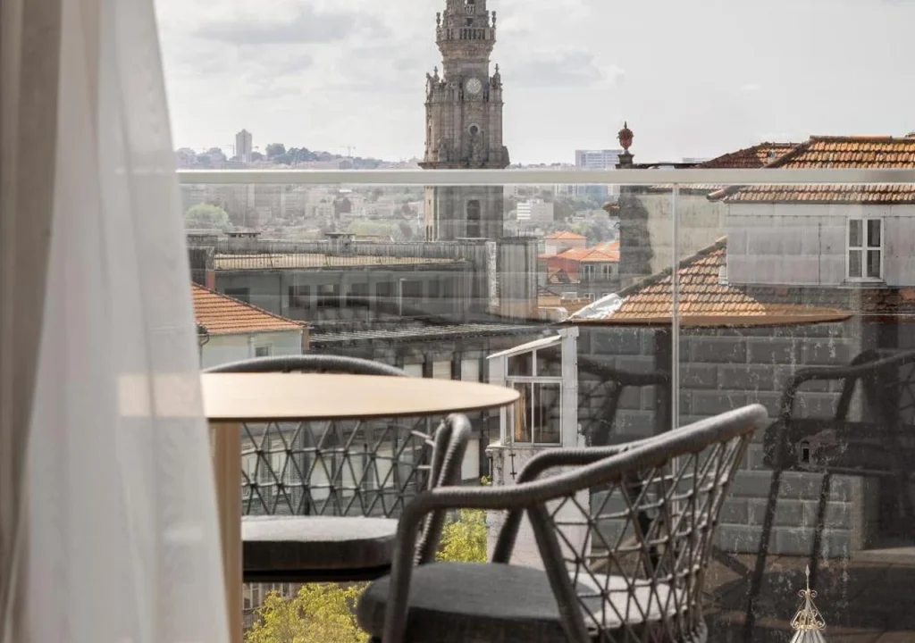 Rooftop terrace with cityscape view and historic clock tower in the distance, framed by a table and chairs.